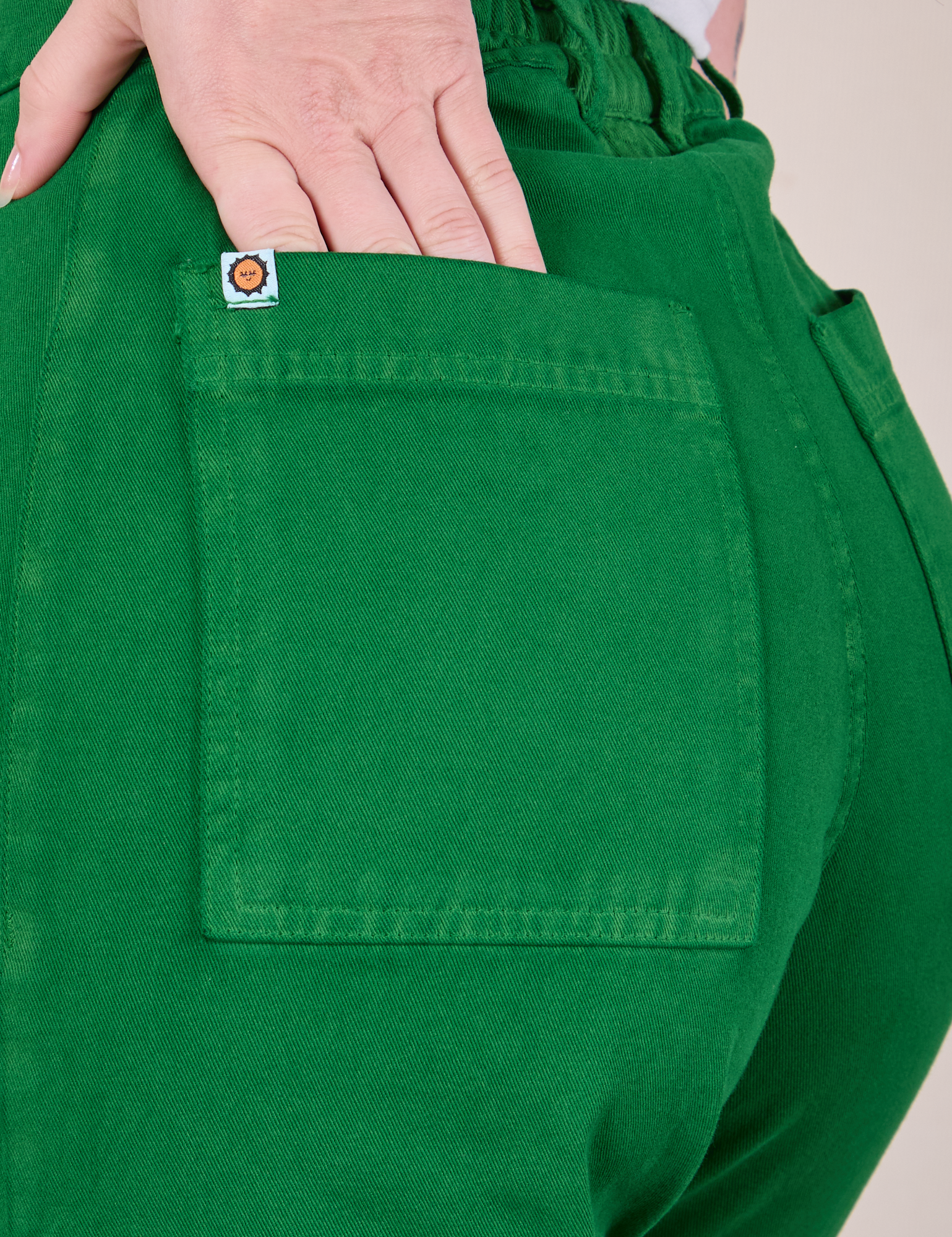 Close up of Alex&#39;s hand in the back pocket of Western Pants in Forest Green