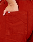 Back pocket close up of Western Pants in Paprika. Alicia has her hand in the pocket. Sun baby logo tag in white and orange on top edge of pocket.