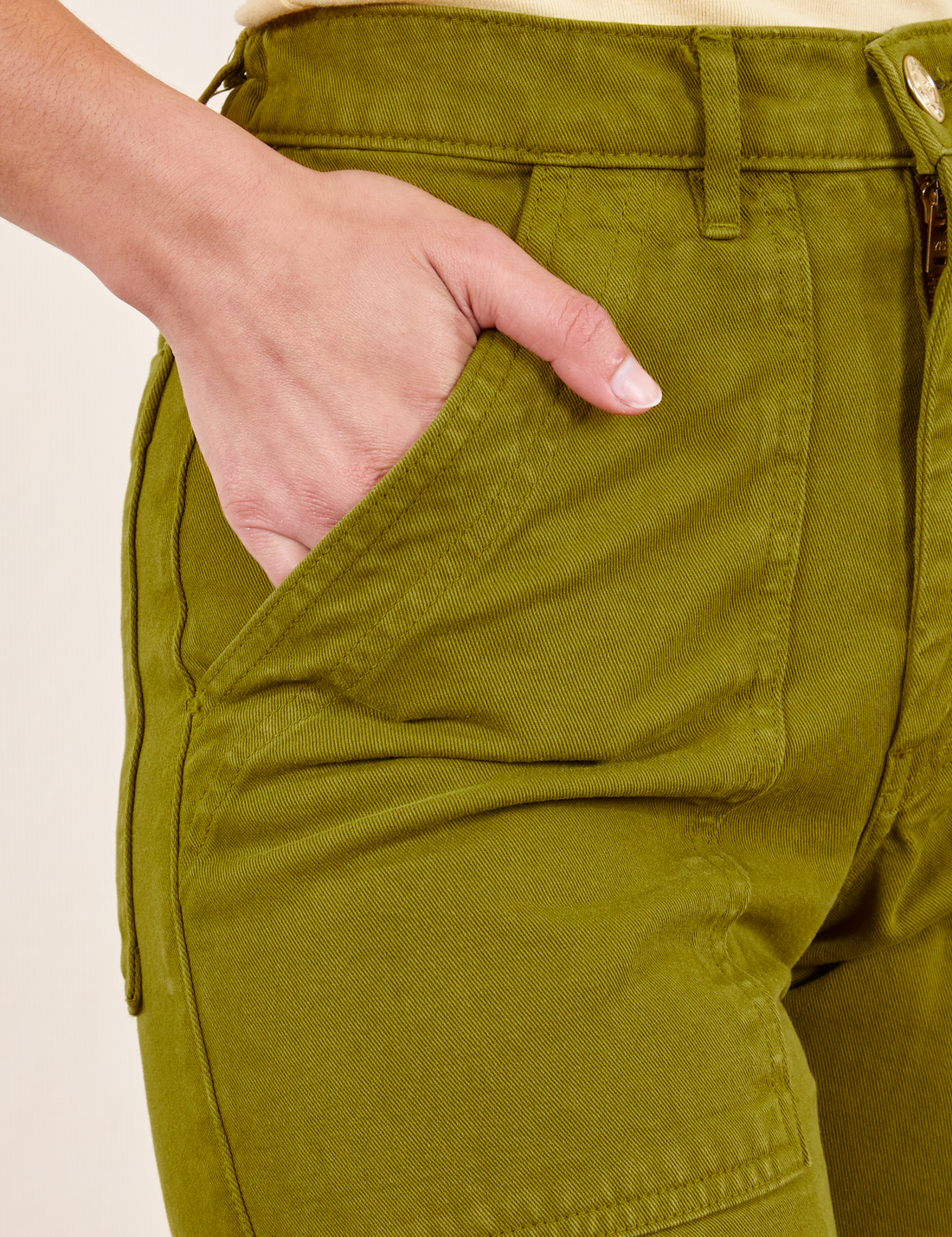 Front pocket close up of Work Pants in Olive Green. Worn by Soraya with her hand in the pocket.