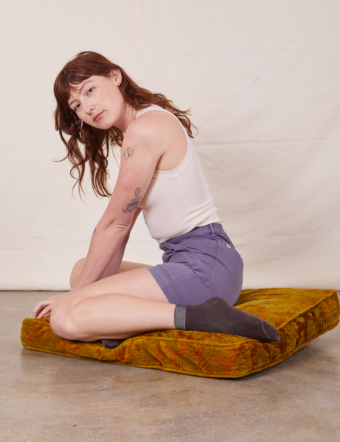 Alex is sitting on a cushion wearing Classic Work Shorts in Faded Grape and vintage off-white Tank Top