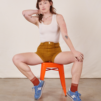 Alex is wearing Classic Work Shorts in Spicy Mustard and vintage off-white Tank Top. She is sitting on a orange metal stool.