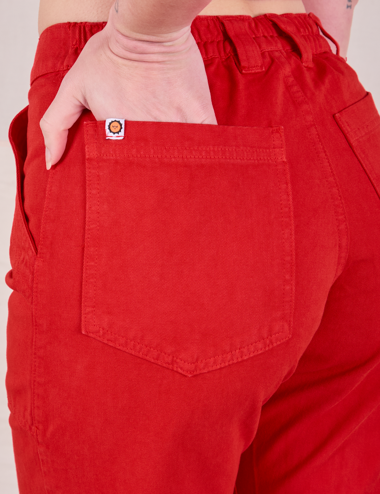 Close up of Alex&#39;s hand in the back pocket of Mid-Rise Work Pants in Mustang Red