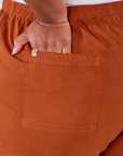 Action Pants in Burnt Terracotta back pocket close up. Morgan has her hand in the pocket.