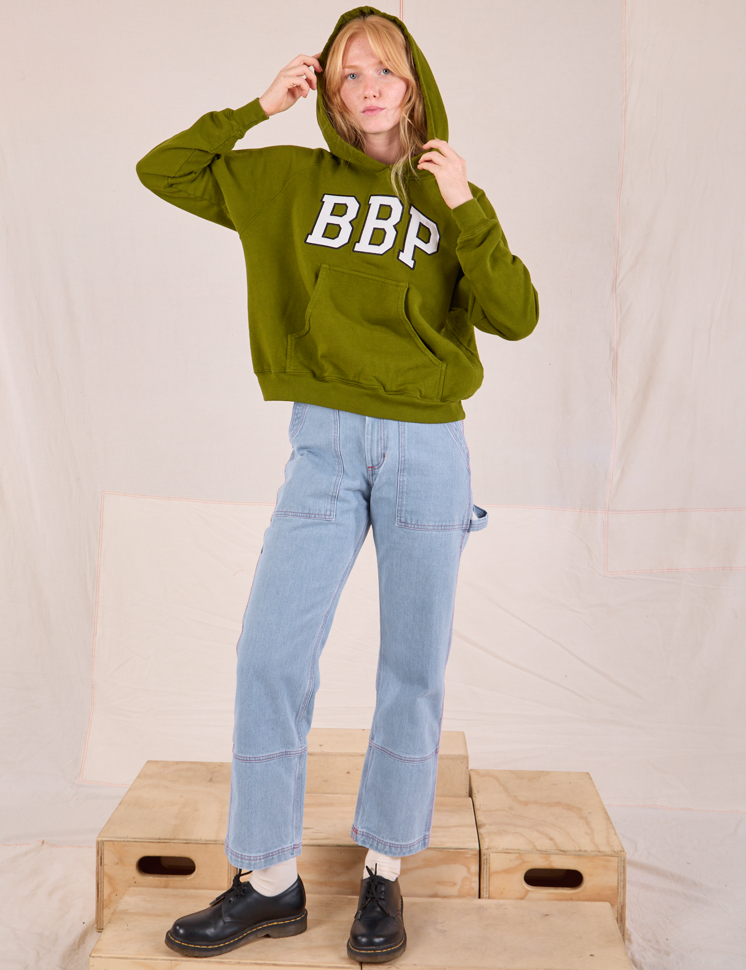 Margaret is wearing Collegiate Hoodie in Summer Olive paired with light wash Carpenter Jeans