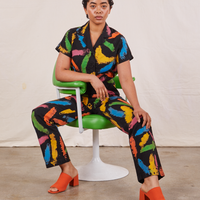 Mika is sitting in a green and white vintage chair. She is wearing Pantry Button Up in Paint Stroke and matching Work Pants.