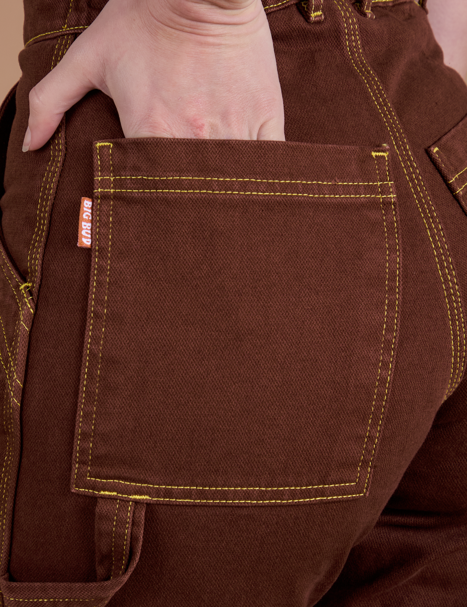 Close up of Alex's hand in the back pocket of Carpenter Jeans in Fudgesicle Brown