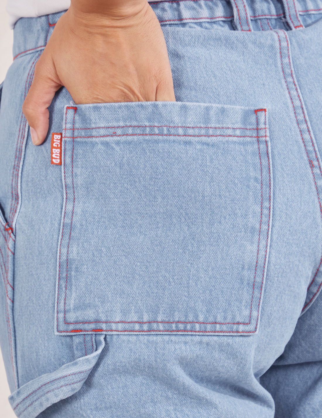 Back pocket close up of Carpenter Jeans in Light Wash. Tiara has her hand tucked into the pocket.