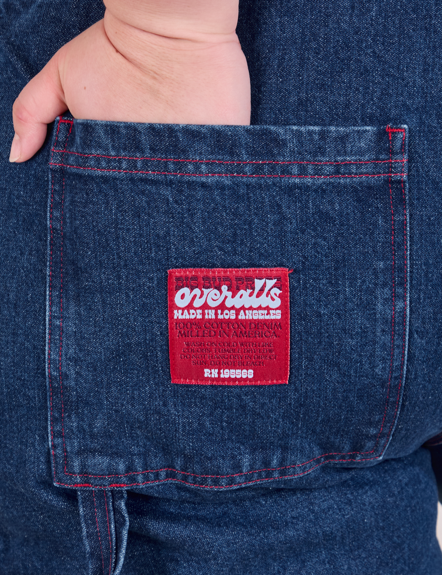 Close up of Ashley&#39;s hand in the back pocket of Carpenter Overalls in Dark Wash