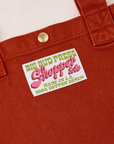 Close up of brass sun baby snap on paprika Shopper Tote Bag. Bag label with green and pink text that reads "Big Bud Press, Shopper Tote, Made in L.A. 100% Cotton Denim" on a white background