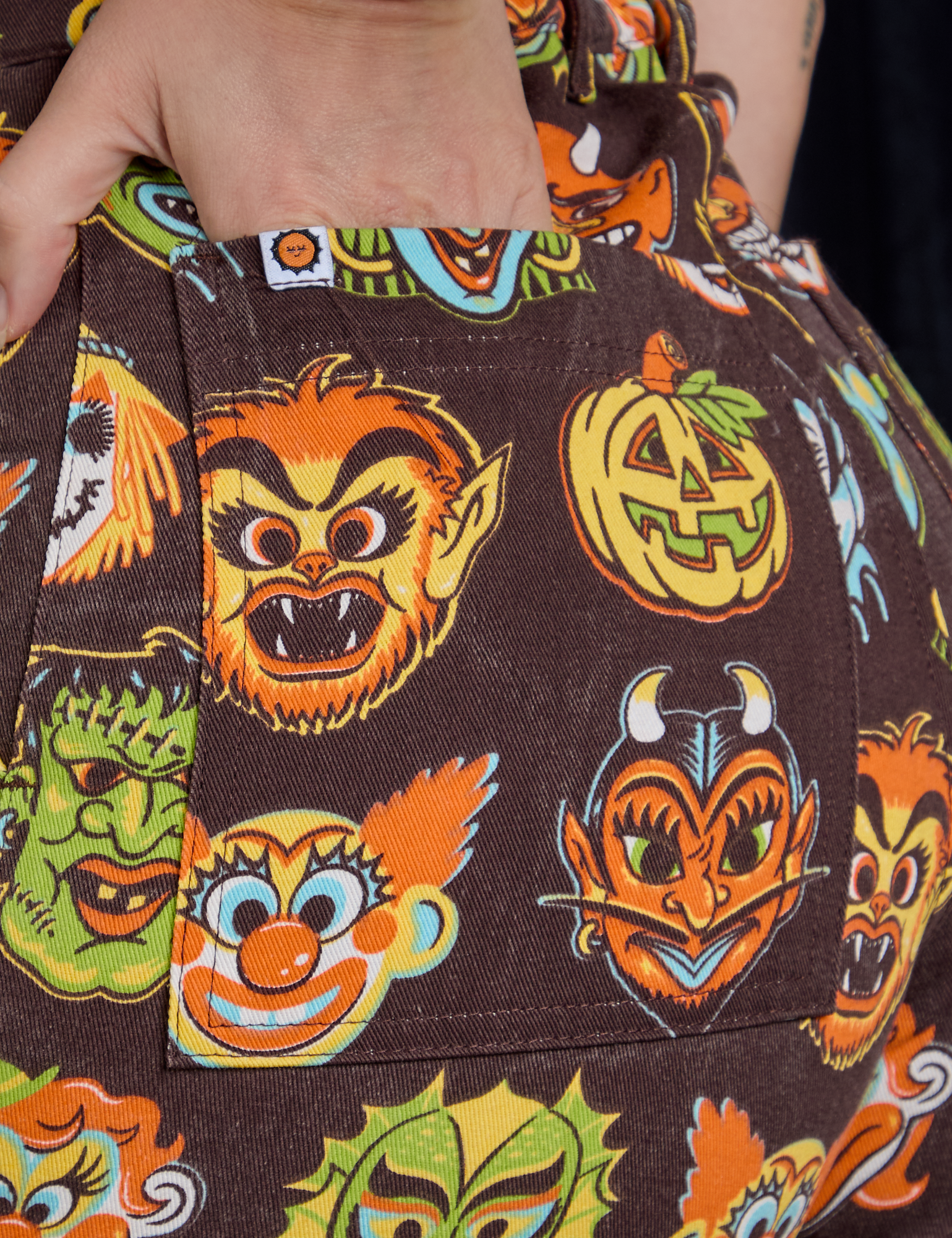 Close up of Alex&#39;s hand in the back pocket of Short Sleeve Jumpsuit in Halloween Masks