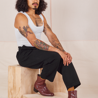 Jesse is sitting on a wooden crate wearing Heavyweight Trousers in Basic Black and vintage off-white Cropped Tank Top.