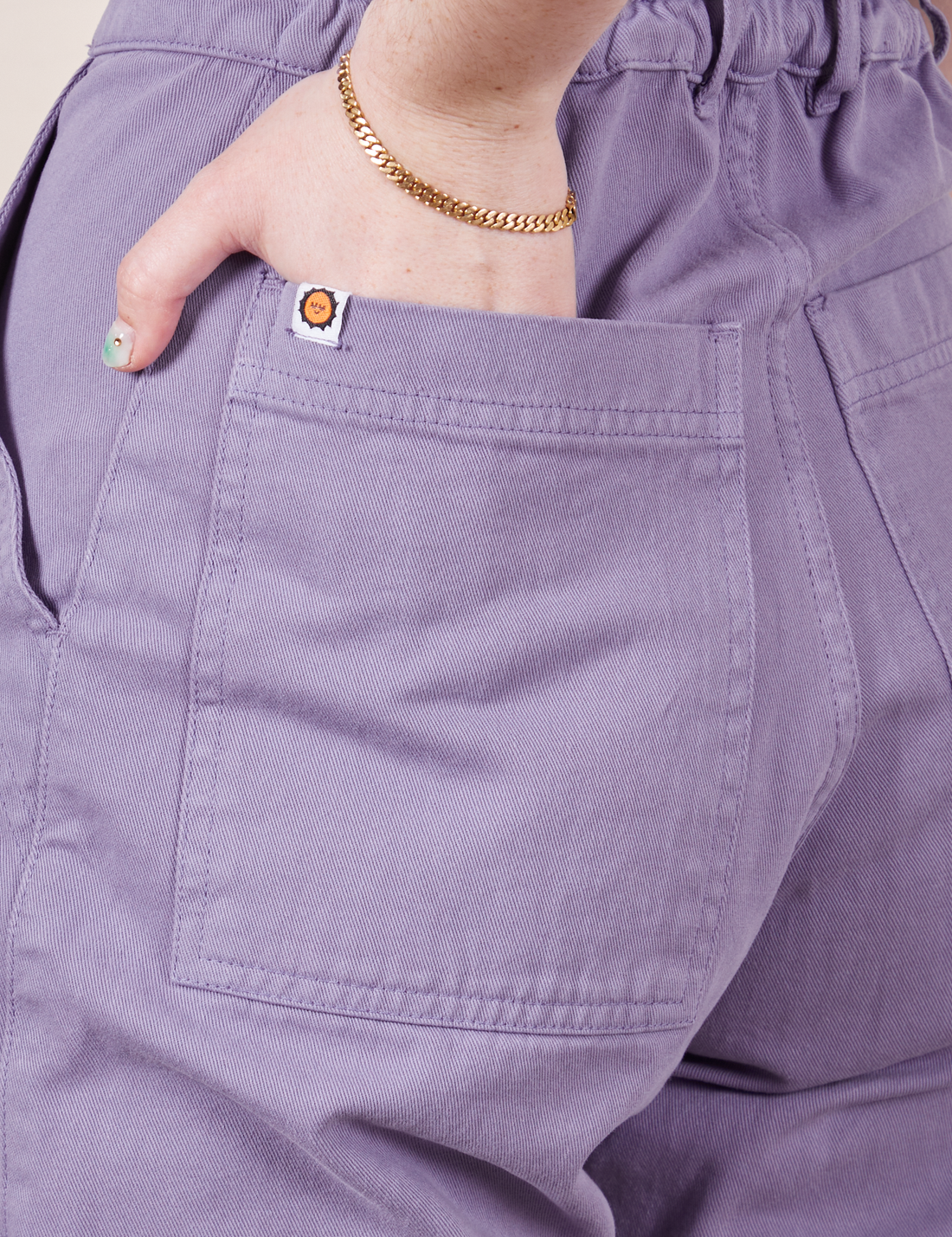 Back pocket close up of Petite Short Sleeve Jumpsuit in Faded Grape. Hana has their hand in the pocket.