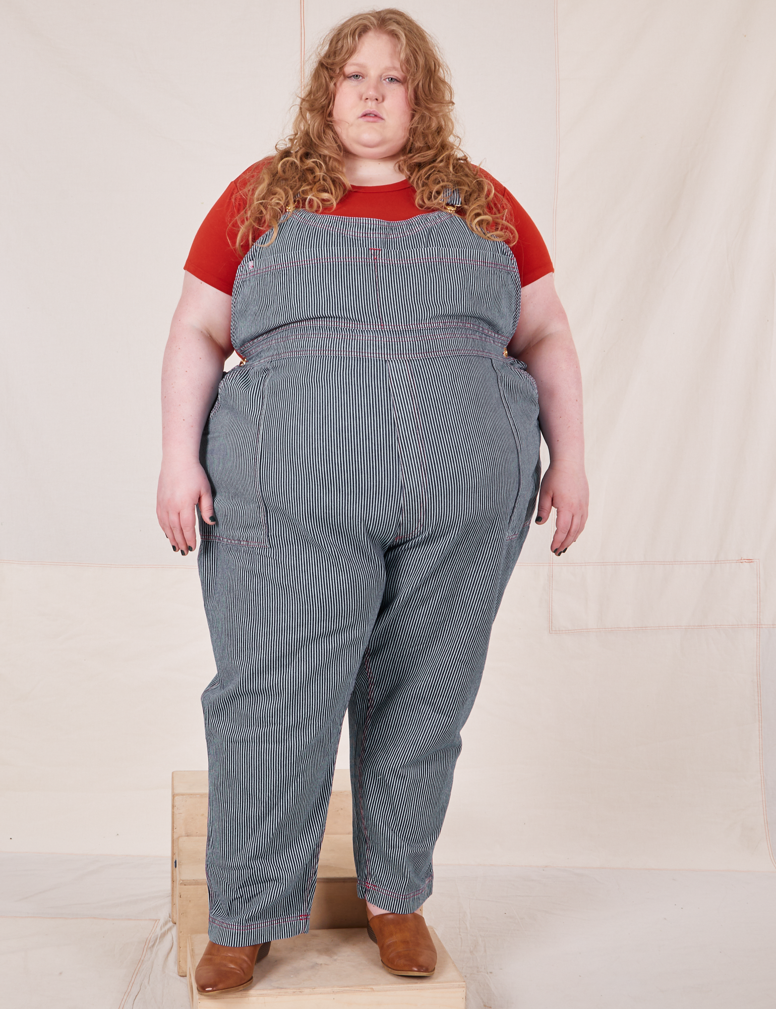 Catie is 5&#39;11&quot; and wearing 5XL Railroad Stripe Denim Original Overalls paired with paprika Baby Tee