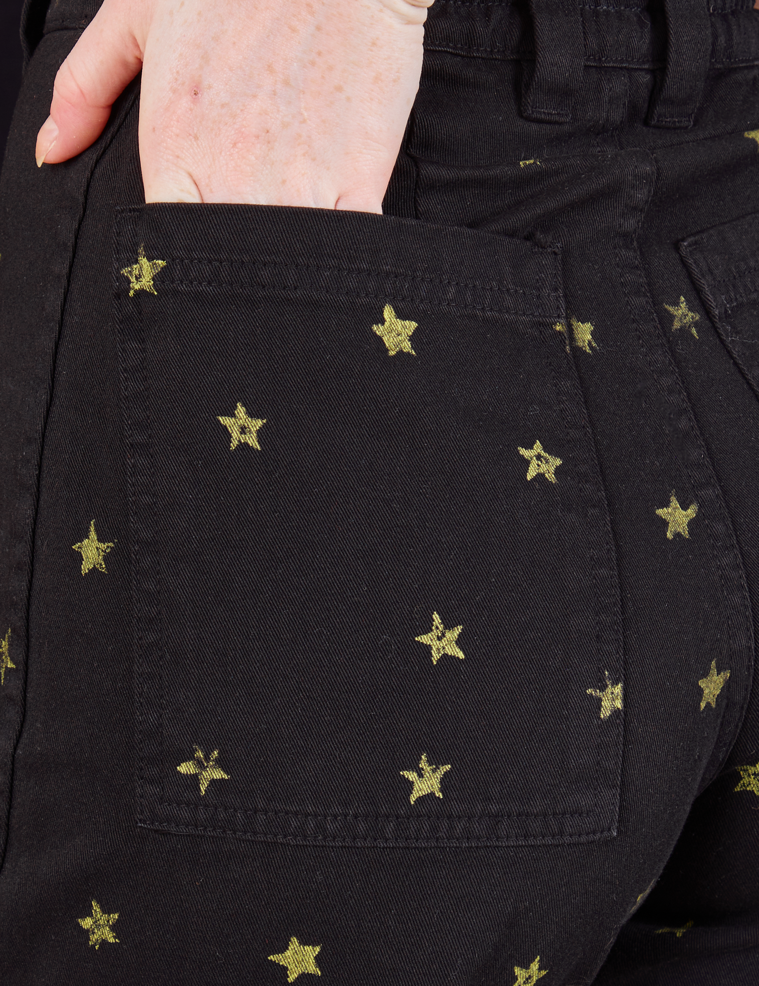 Star Bell Bottoms in Black back pocket close up. Margaret has her hand in the pocket.