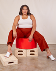 Alicia is sitting on a circular platform wearing Western Pants in Paprika and a vintage off-white Tank Top