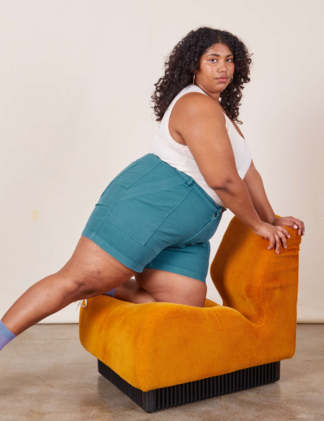 Morgan is kneeling on a upholstered chair wearing Classic Work Shorts in Marine Blue and vintage off-white Tank Top