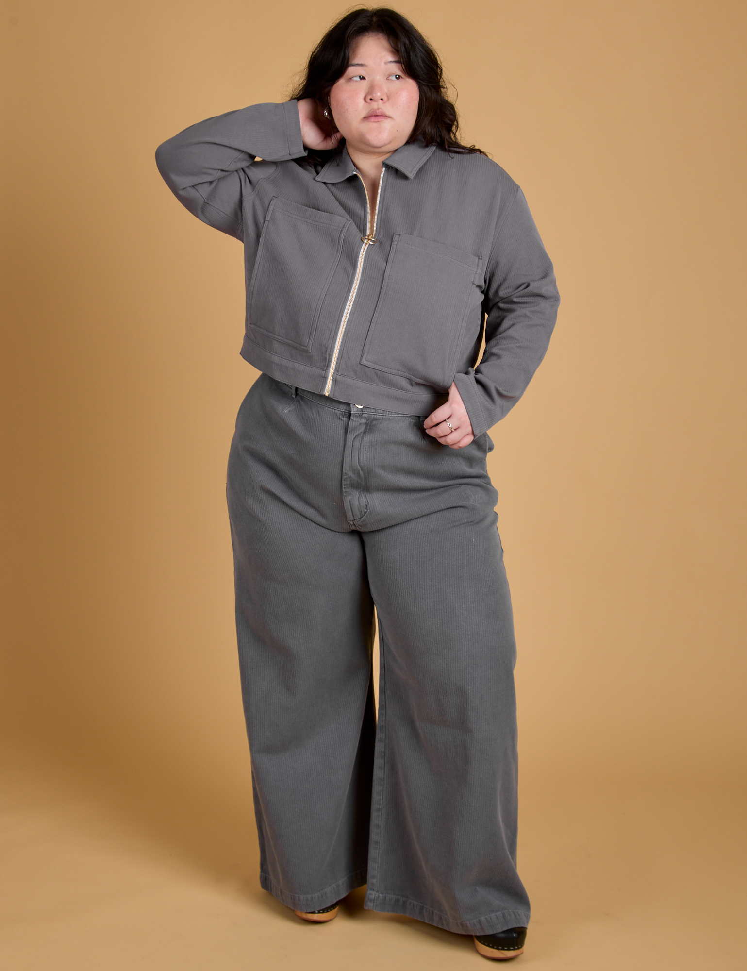 Ashley is wearing a zipped up Heritage Mechanic Jacket in Washed Grey paired with matching Wide Leg Trousers