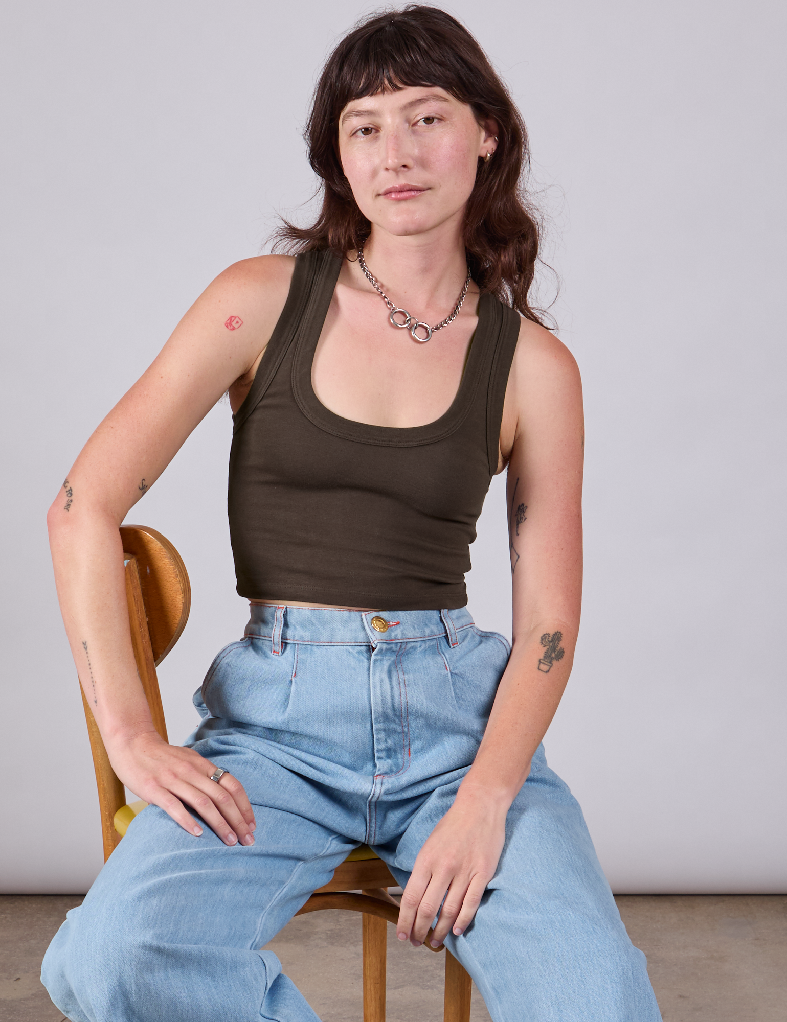 Alex is sitting in a chair wearing Cropped Tank Top in Espresso Brown paired with light wash Indigo Wide Leg Trousers