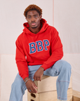 Issac is wearing Collegiate Hoodie in Mustang Red and light wash Carpenter Jeans