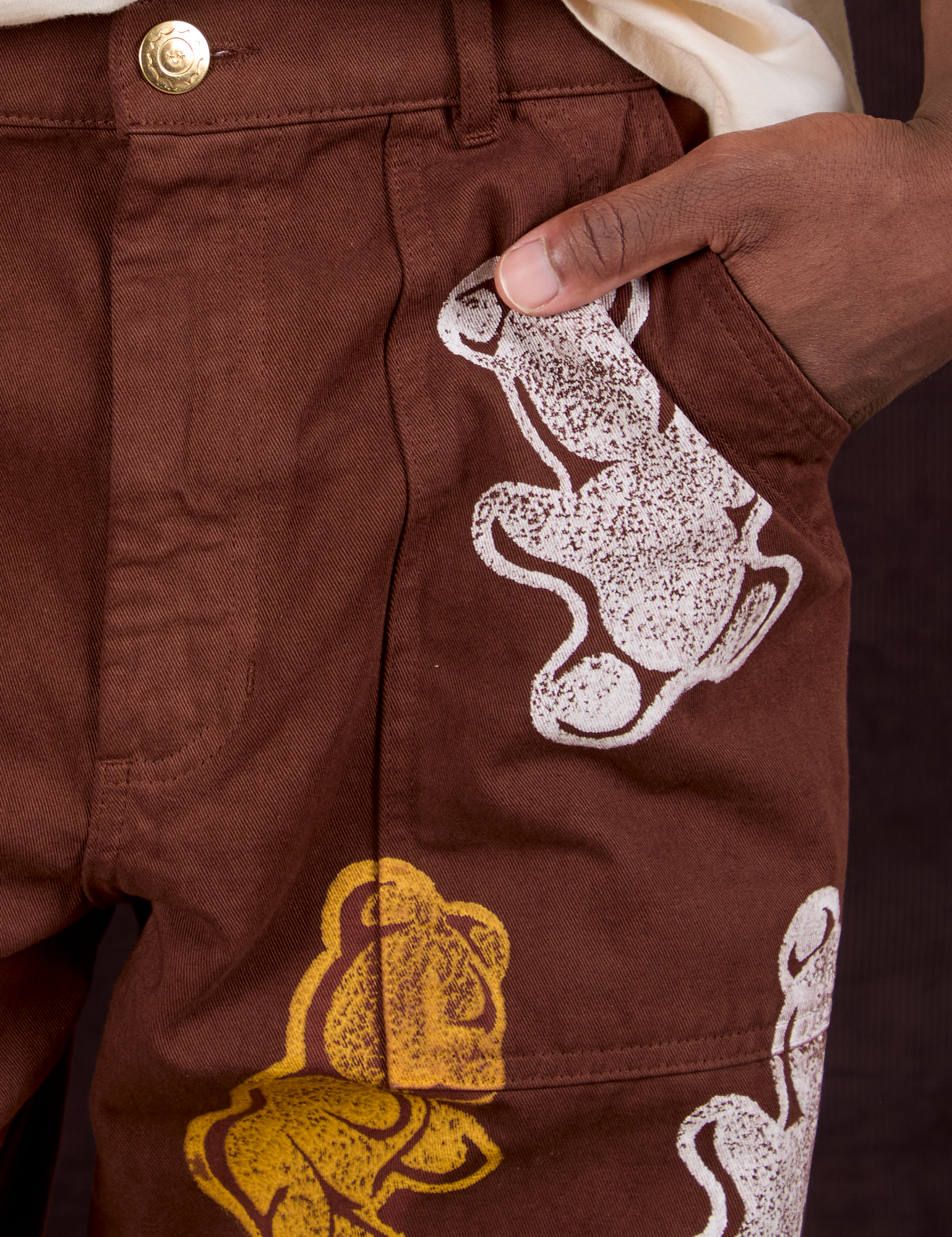 Close up of Isaac&#39;s hand in the front pocket of Gummy Bear Paintstamped Work Pants in Fudgesicle Brown