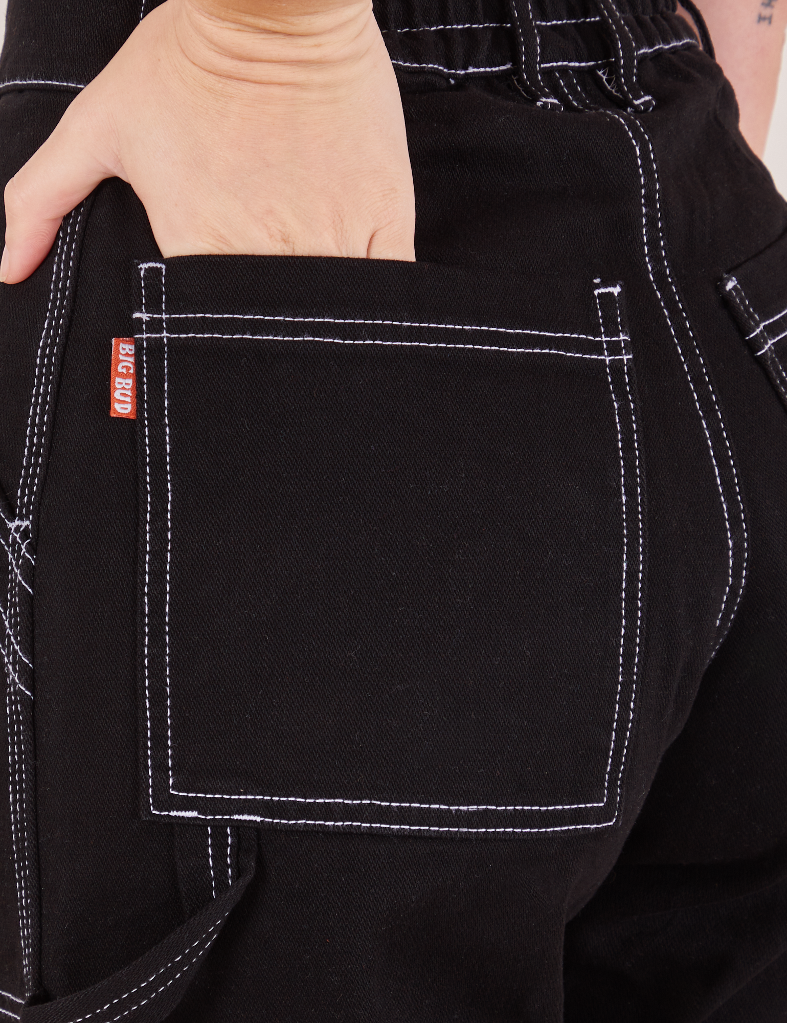 Back pocket close up of Carpenter Jeans in Black. Alex has her hand in the pocket. Pocket has a contrast white top stitching along the edges
