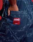 Meghna has her hand in the back pocket of Carpenter Overalls in Chain Link