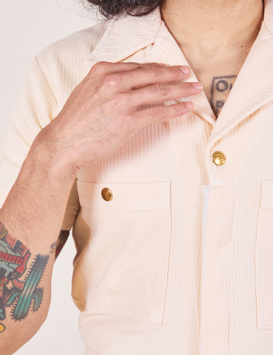 Front close up of Heritage Short Sleeve Jumpsuit in Natural. Jesse has their hand on the collar