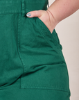 Front pocket close up of Petite Short Sleeve Jumpsuit in Hunter Green. Ashley has her hand in the pocket.