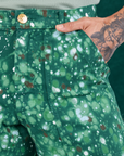 Front pocket close up of Marble Splatter Work Pants in Hunter Green. Jesse has their hand in the pocket.