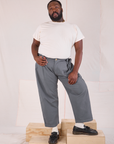 Elijah is 6'3" and wearing 1XL Mid-Rise Pleated Trousers in Slate Grey paired with an Organic Vintage Tee in vintage tee off-white