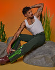 Jesse is sitting on a boulder. They are wearing Paintstamped Work Pants in Cactus and a Cropped Tank in Vintage Tee White