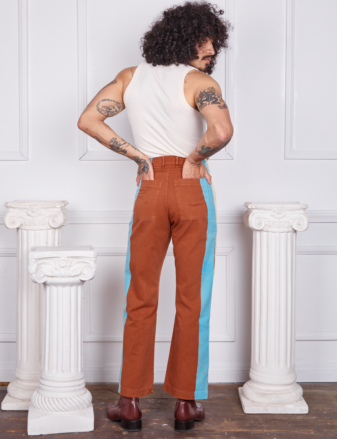 Back view of Hand-Painted Stripe Western Pants in Burnt Terracotta and vintage off-white Tank Top worn by Jesse. They also have both their hands in the back pockets