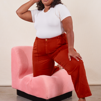 Work Pants in Paprika on Morgan wearing a vintage off-white Baby Tee. Morgan has one knee on a pink upholstered chair and the other leg on the ground.