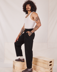 Side view of Denim Trouser Jeans in Black and vintage off-white Tank Top worn by Jesse