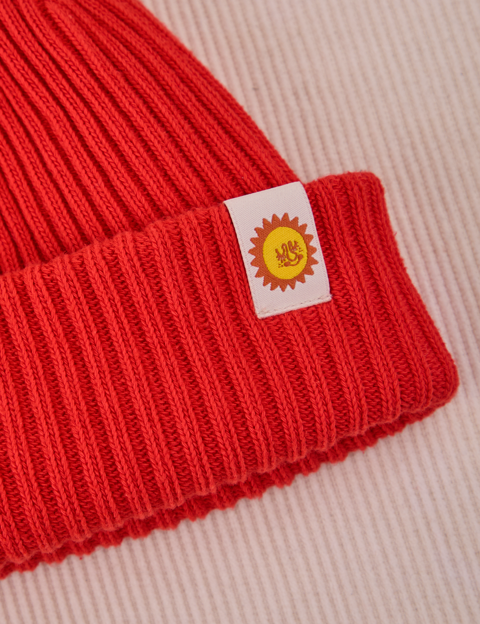 Ribbed Beanie in Mustang Red close up of sun logo