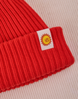 Ribbed Beanie in Mustang Red close up of sun logo