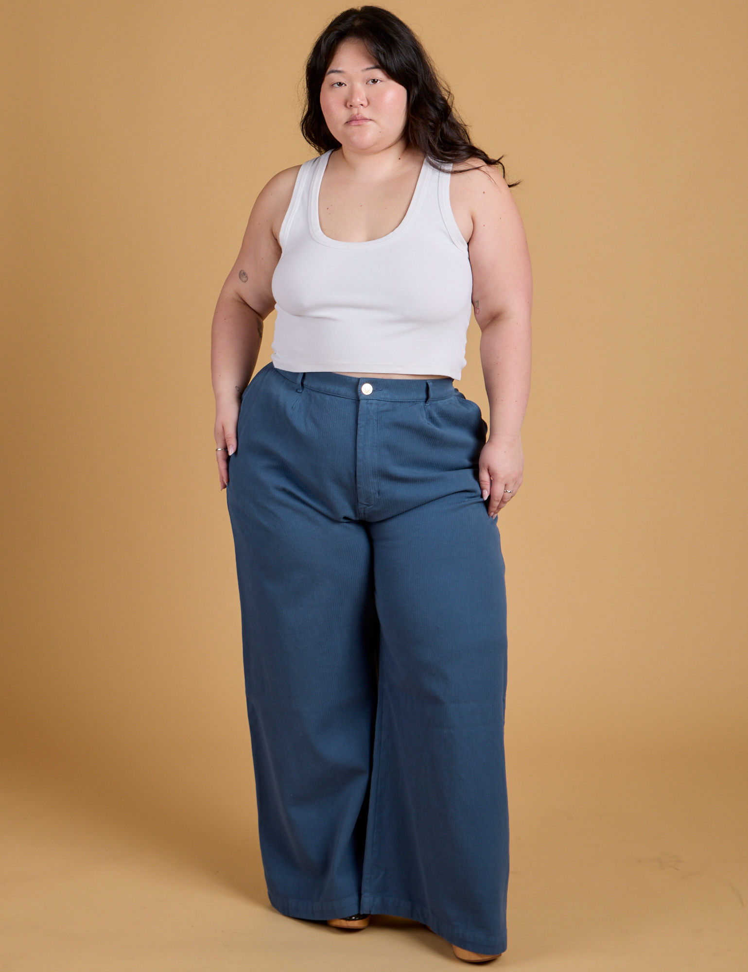 Ashley is 5&#39;7&quot; and wearing 1XL Heritage Wide Leg Trousers in French Blue paired with a vintage tee white Cropped Tank