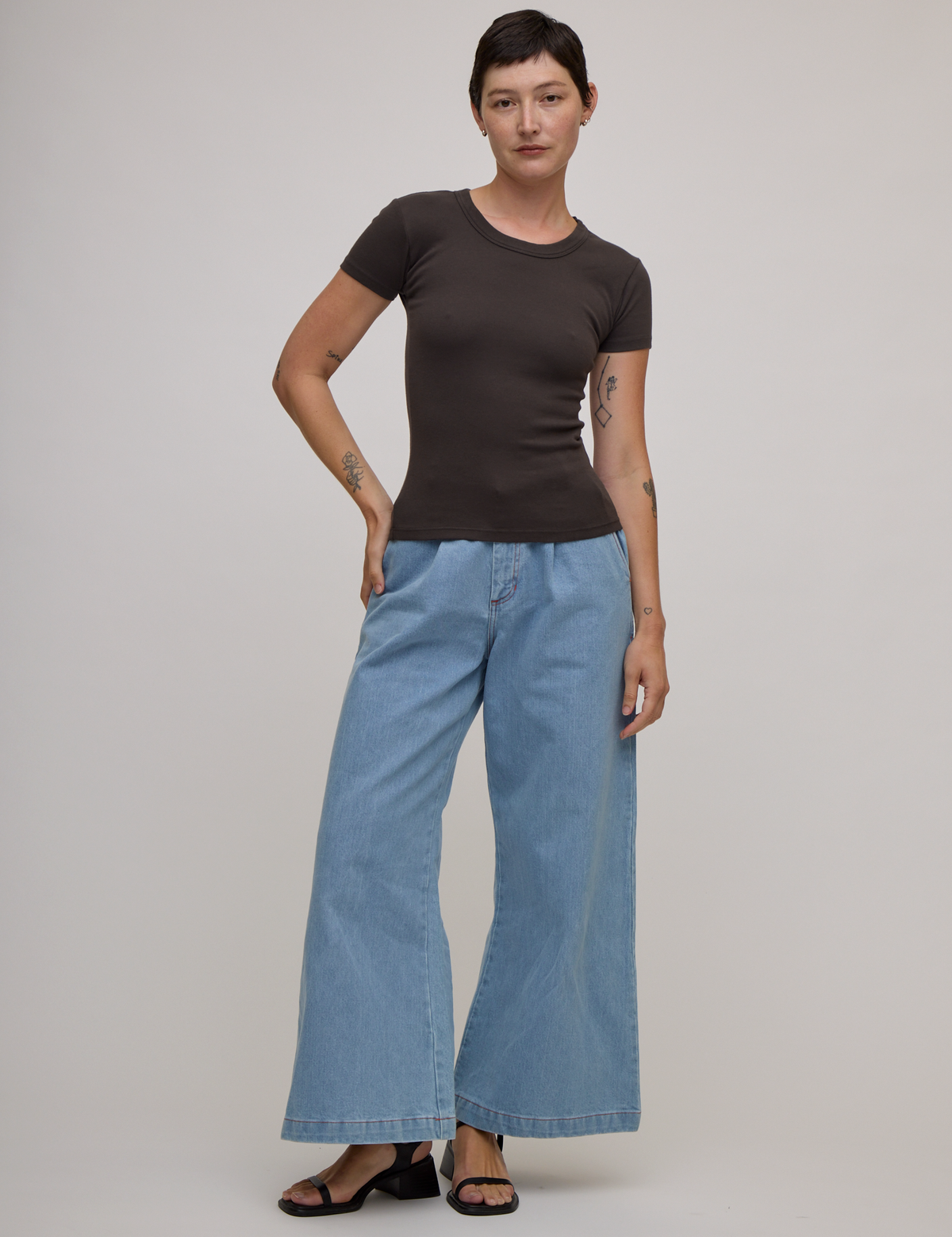 Alex is 5'8" and wearing P Baby Tee in Espresso Brown paired with light wash wide leg denim trousers