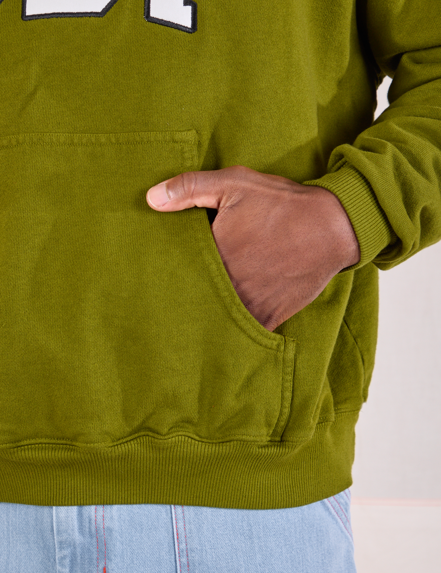 Collegiate Hoodie in Summer Olive kangaroo pocket close up. Issac has his hand in the pocket.