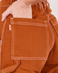 Carpenter Jeans in Burnt Terracotta back pocket close up. Alex has her hand in the pocket.