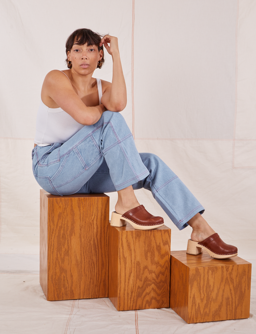 Tiara is sitting on a wooden box wearing Carpenter Jeans in Light Wash