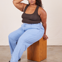 Morgan is wearing Cropped Tank Top in Espresso Brown and light wash Denim Trousers sitting on a wooden box.