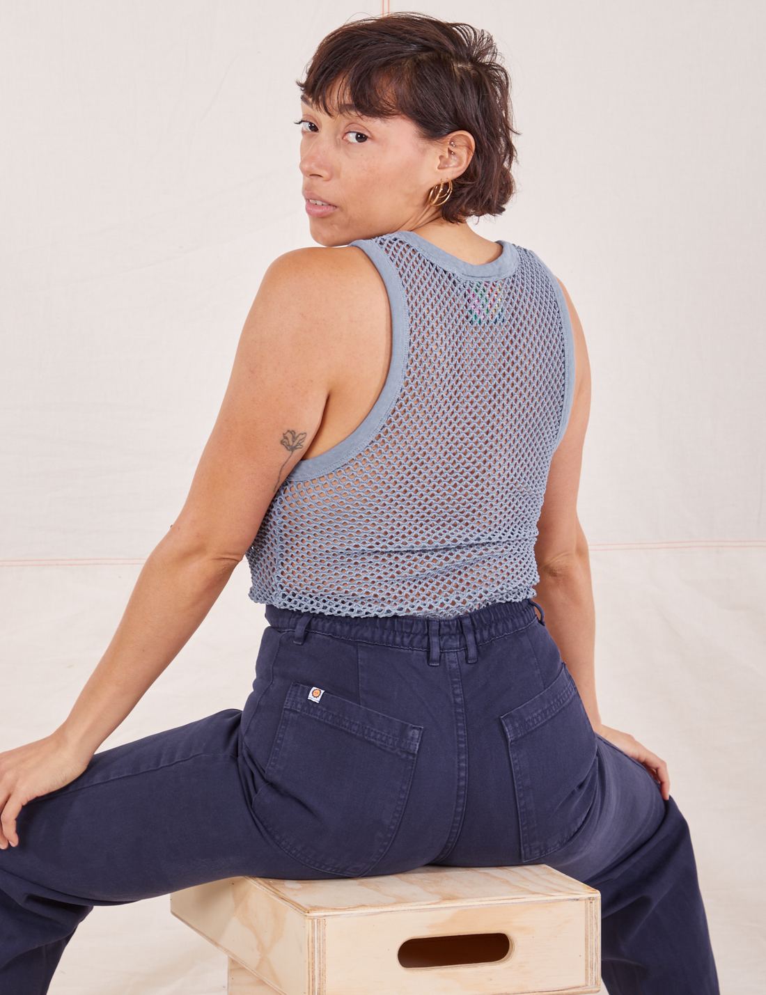 Tiara is sitting on a wooden crate with her back turned. She is wearing Mesh Tank Top in Periwinkle and navy Western Pants