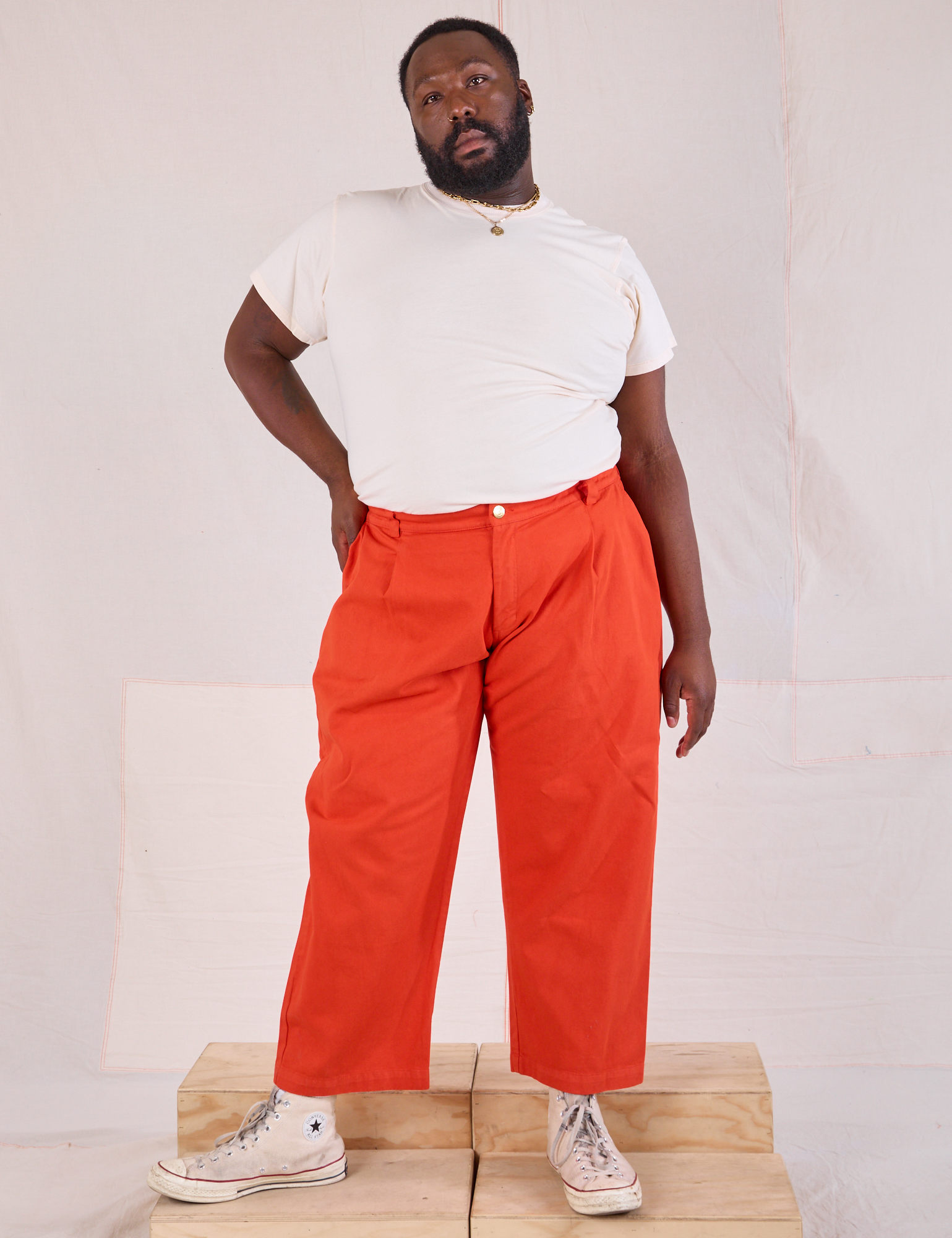 Elijah is wearing Mid-Rise Pleated Trousers in Chili Red and Organic Vintage Tee in vintage tee off-white