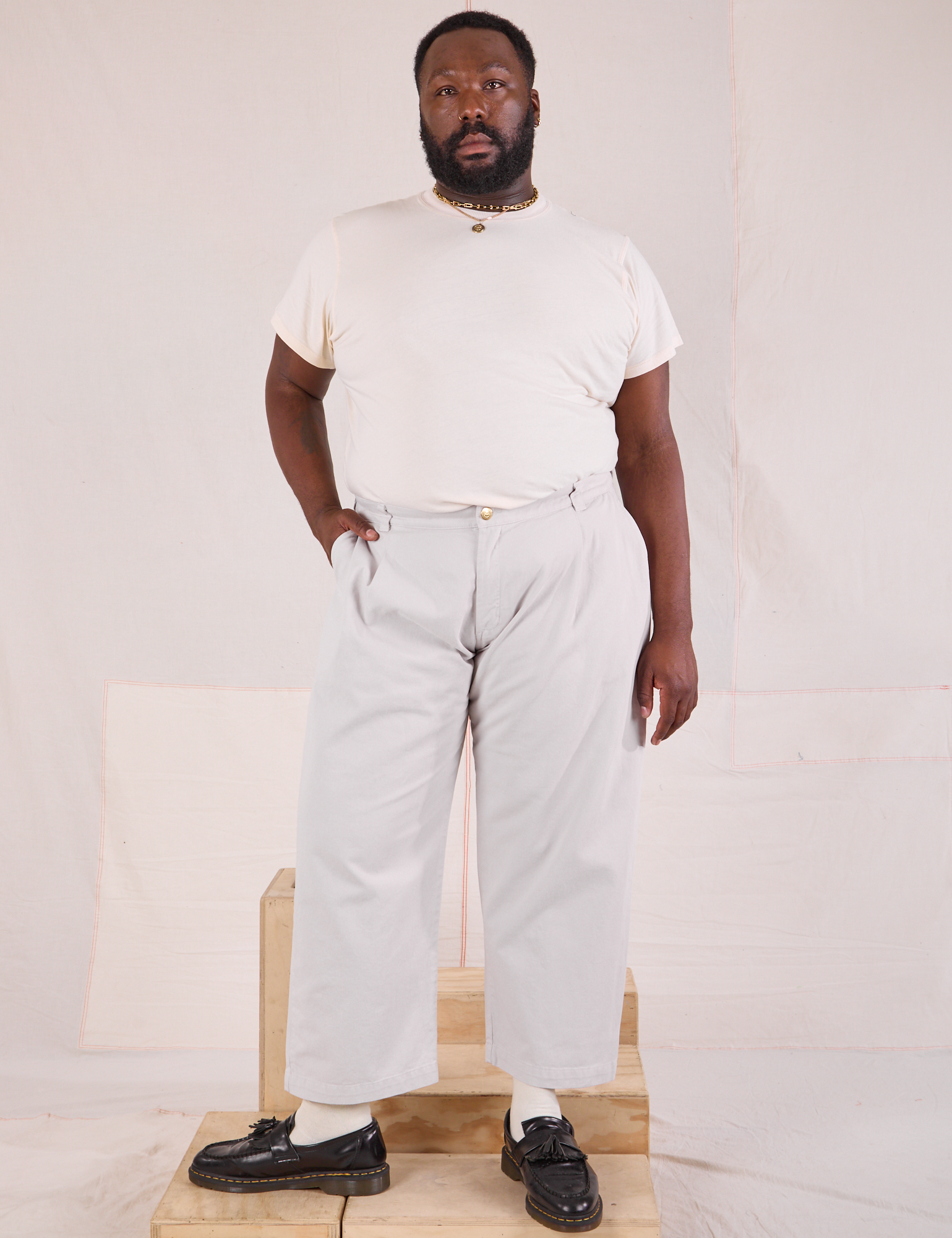 Elijah is 6&#39;3&quot; and wearing 1XL Mid-Rise Pleated Trousers in Stone White paired with Organic Vintage Tee in vintage tee off-white