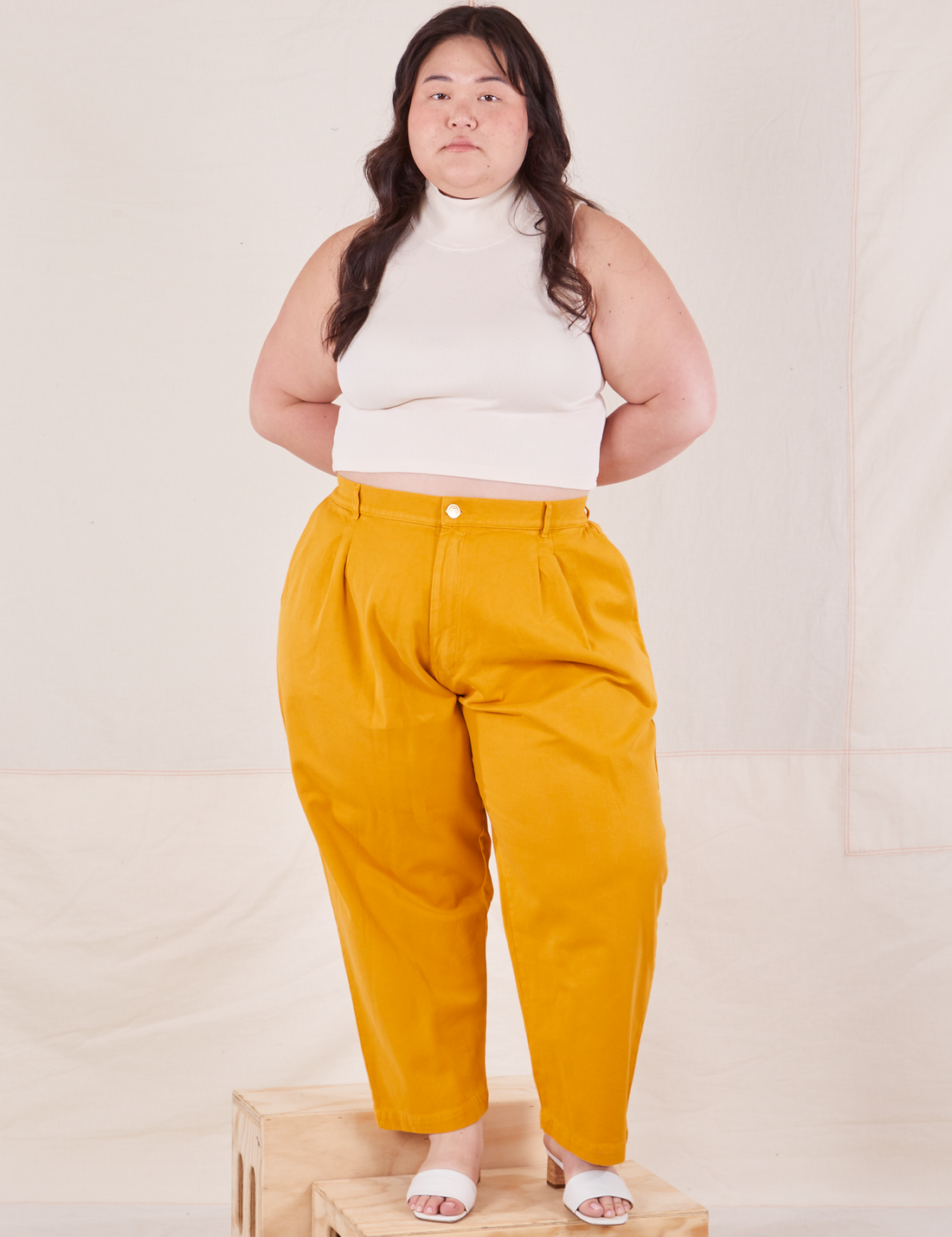 Ashley is 5'7" and wearing 1XL Petite Organic Trousers in Mustard Yellow paired with vintage off-white Sleeveless Essential Turtleneck