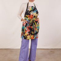 Tiara is wearing Artist Togs Full Apron in Rainbow Magic Waters and has both hands in the apron pockets. She is wearing a vintage off-white Essential Turtleneck and faded grape Western Pants underneath.