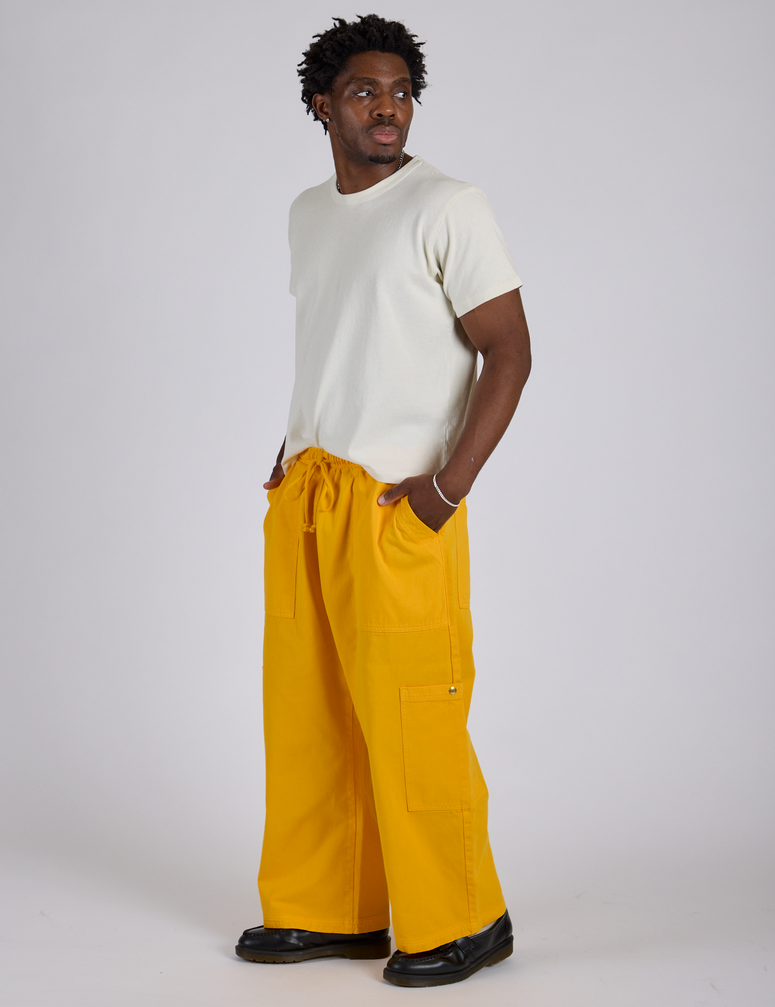 Angled front view of Drop Pocket Cargo Pants in Sunshine Yellow and Organic Vintage Tee in Vintage Tee White on Isaac