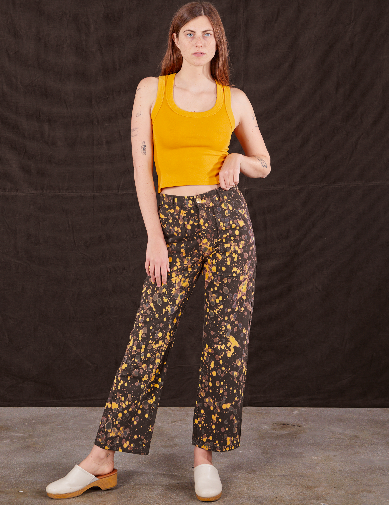 Scarlett is 5&#39;9&quot; and wearing XS Marble Splatter Work Pants in Espresso Brown paired with mustard yellow Tank Top