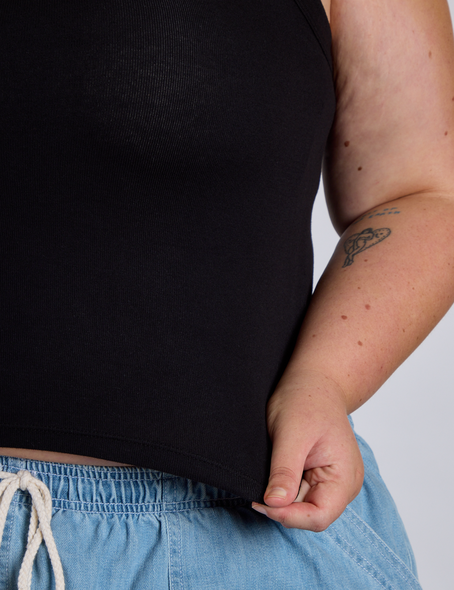 Close up of Juliet holding The Tank Top in Basic Black bottom hem